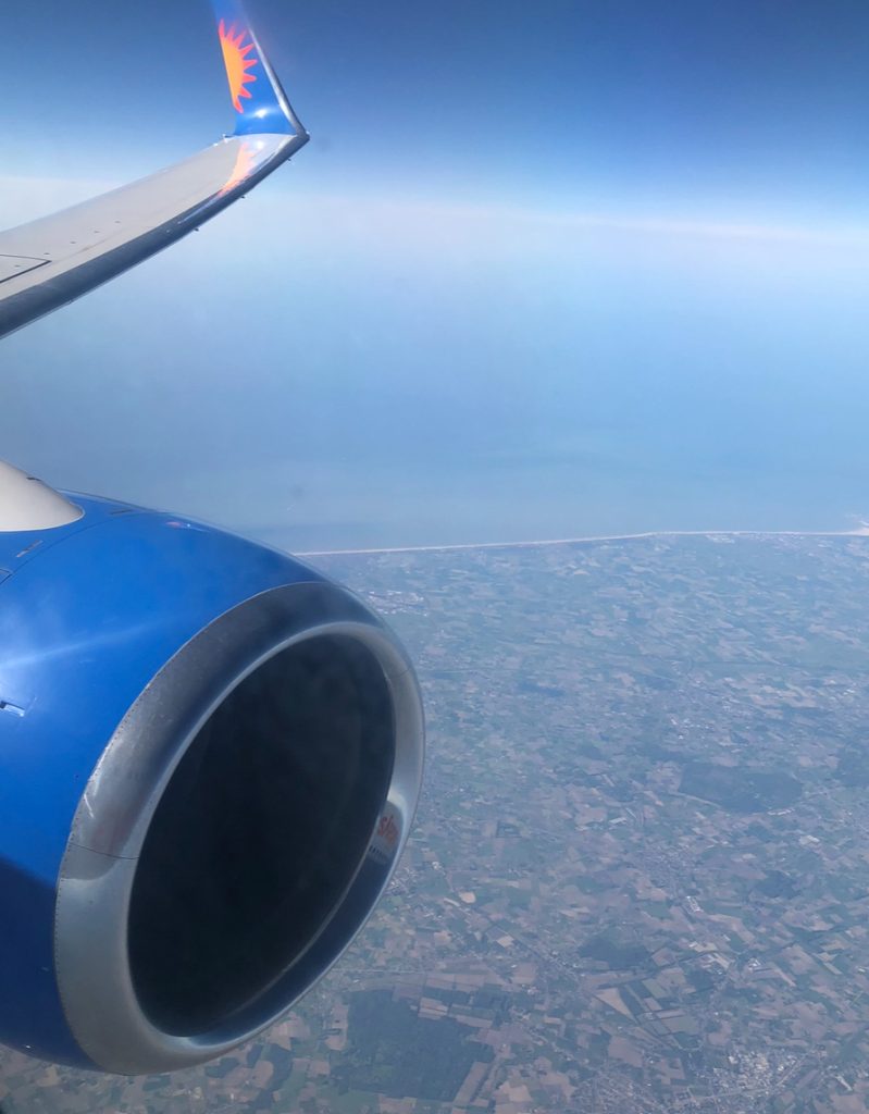 a photo taken out of a plane window, you can see the tip of the plane wing and the jet engine. the sky is blue and clear and below is america.